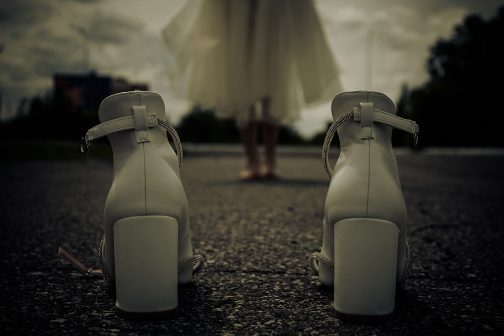 a woman in a white dress standing next to a pair of white high heels