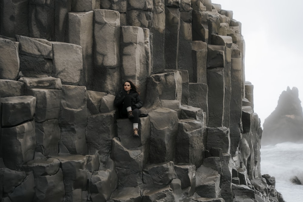 a woman sitting on a rock formation near the ocean