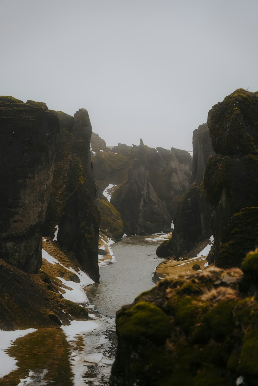 a river surrounded by moss covered rocks in the snow