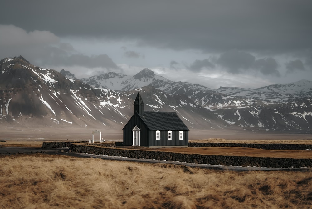 a small black church in a field with mountains in the background
