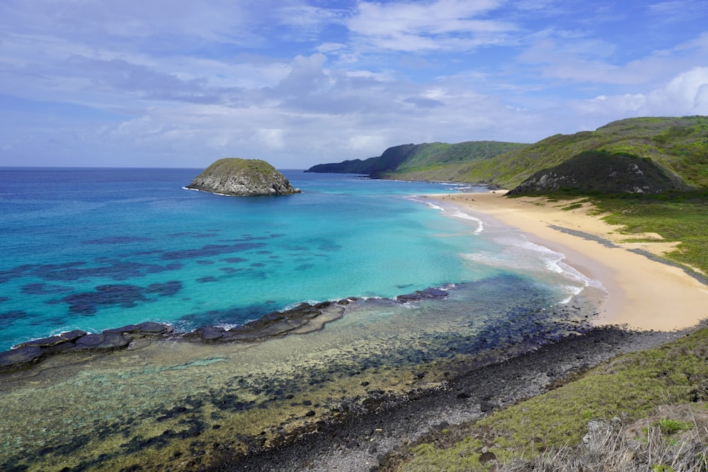 a sandy beach with clear blue water and green hills in the background