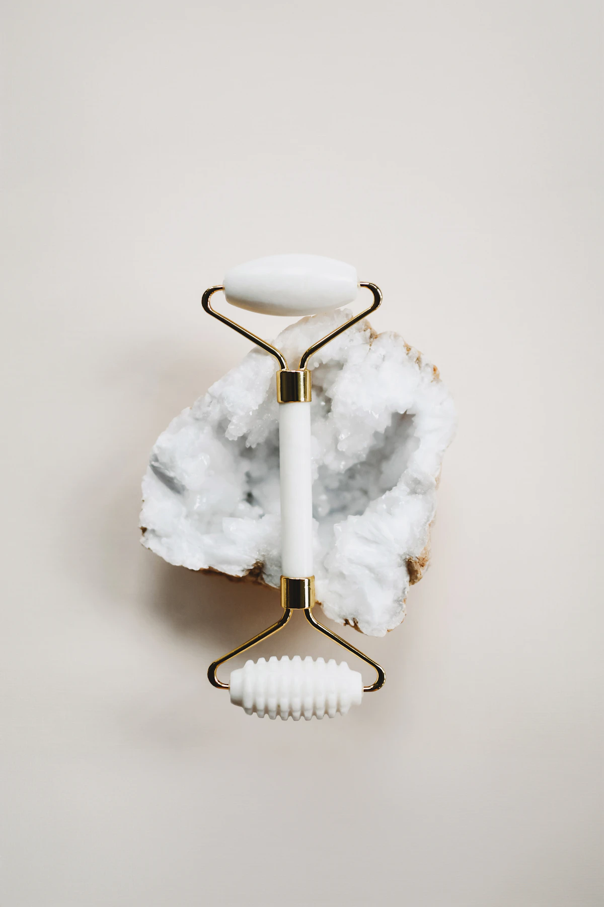 White jade facial roller resting on a quartz crystal