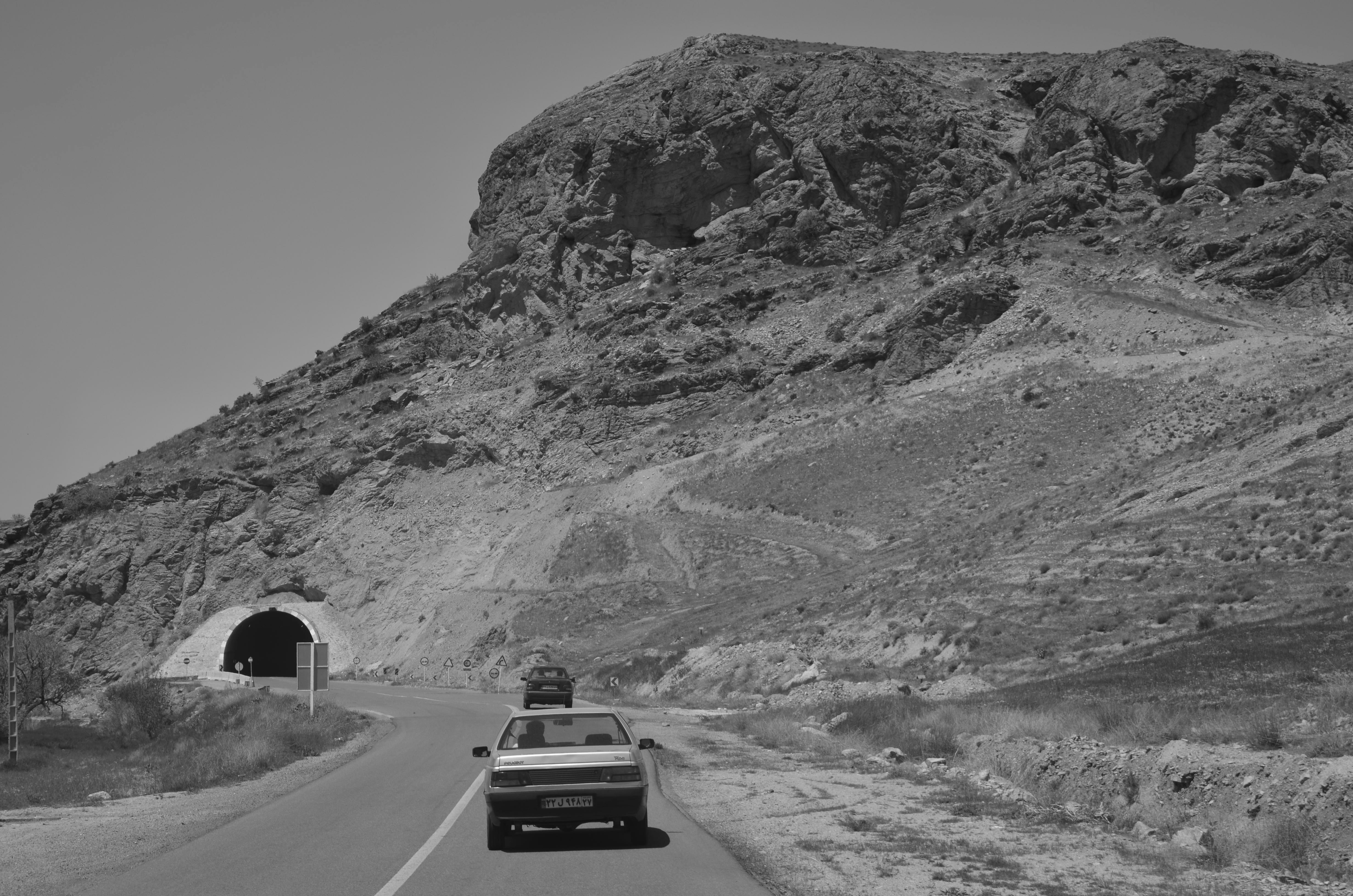 a car driving down a road next to a mountain