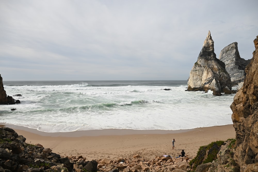 a couple of people standing on top of a sandy beach