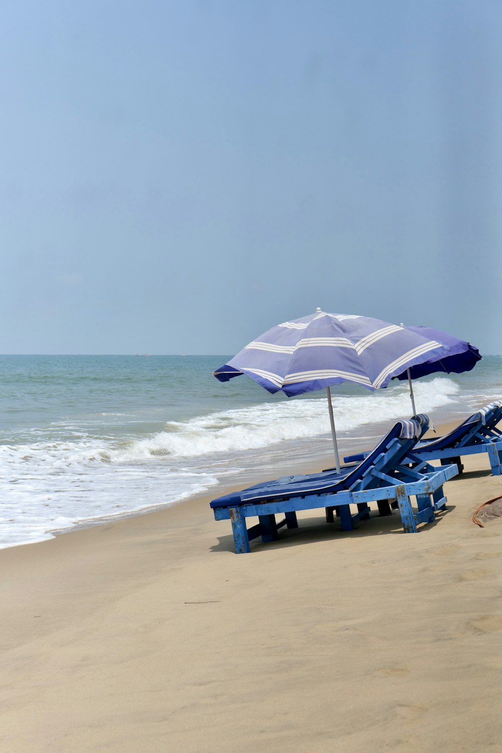 a couple of blue lounge chairs sitting on top of a sandy beach