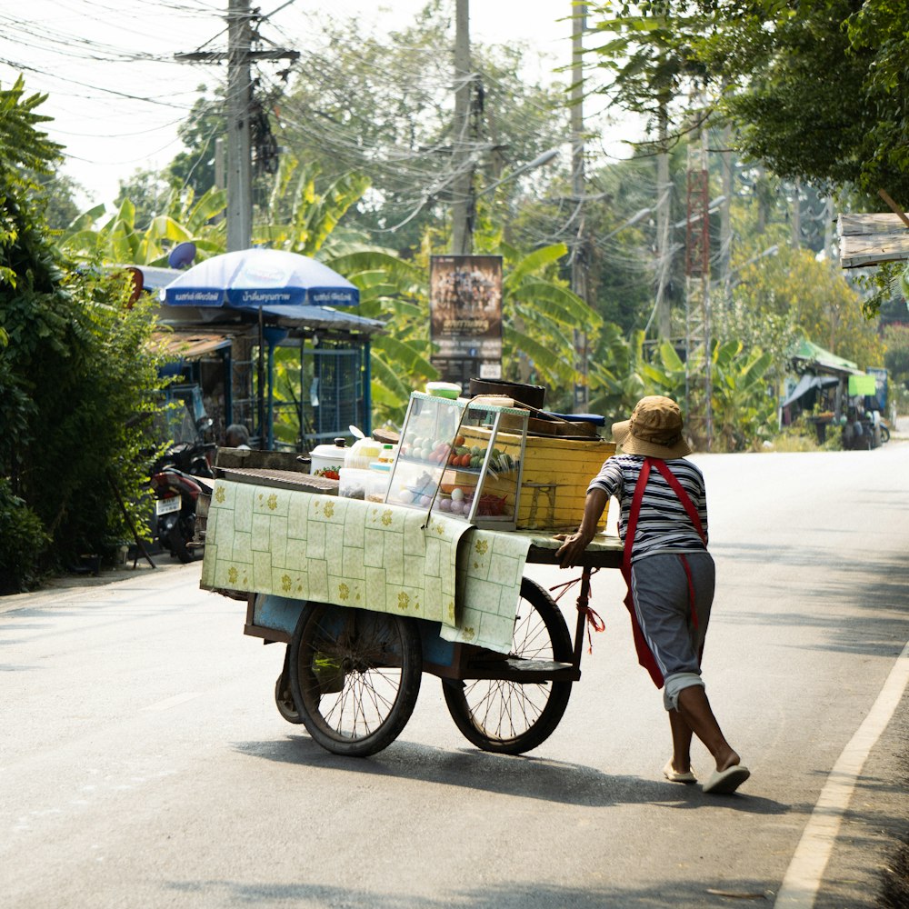 a woman pushing a cart full of items down a street