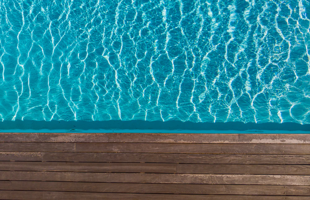 Wooden deck boards along the edge of a bright blue swimming pool