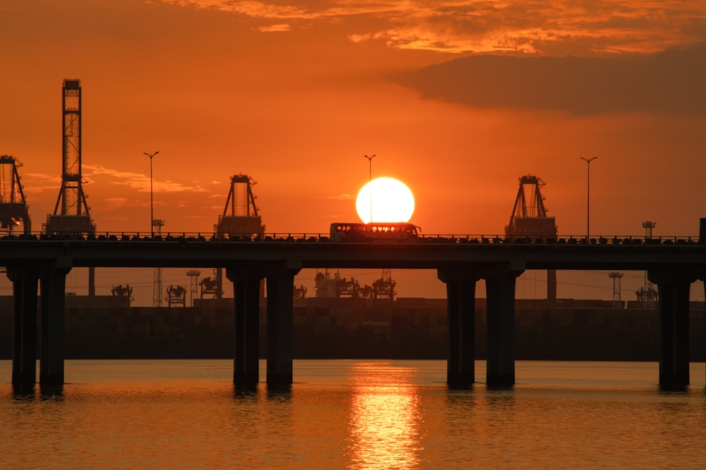 the sun is setting over a bridge over a body of water