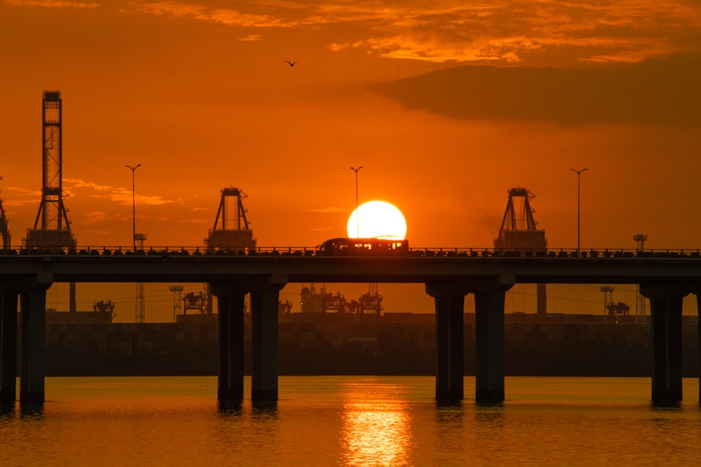 the sun is setting over a bridge over a body of water