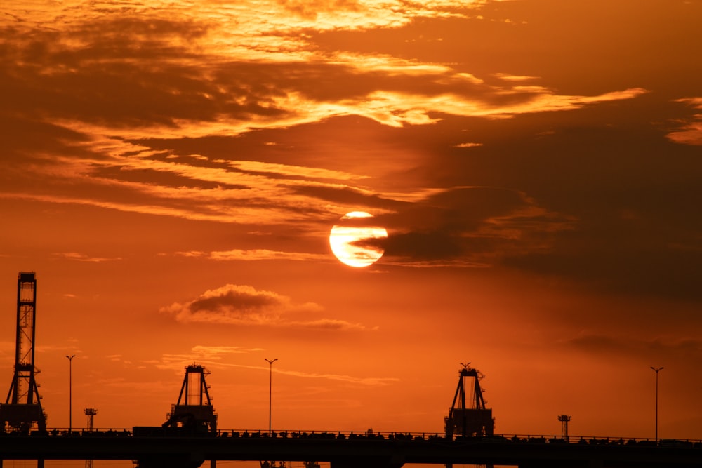 the sun is setting over a bridge with cranes