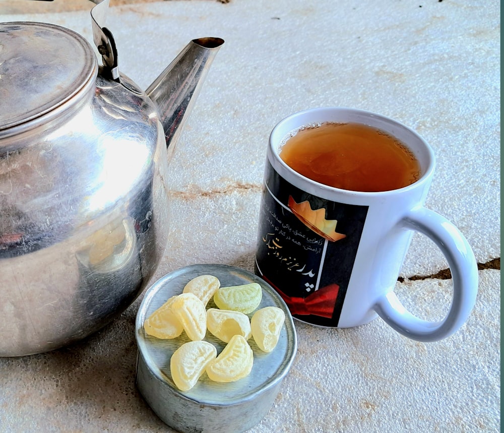 a cup of tea next to a tea pot and a cup of cookies