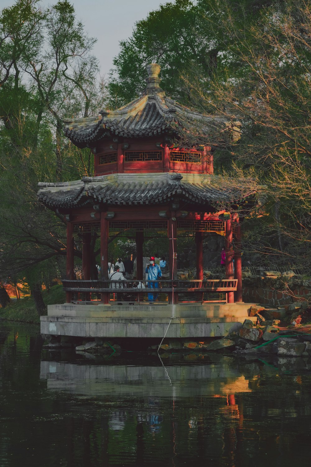 a pavilion with people standing on it in the middle of a lake