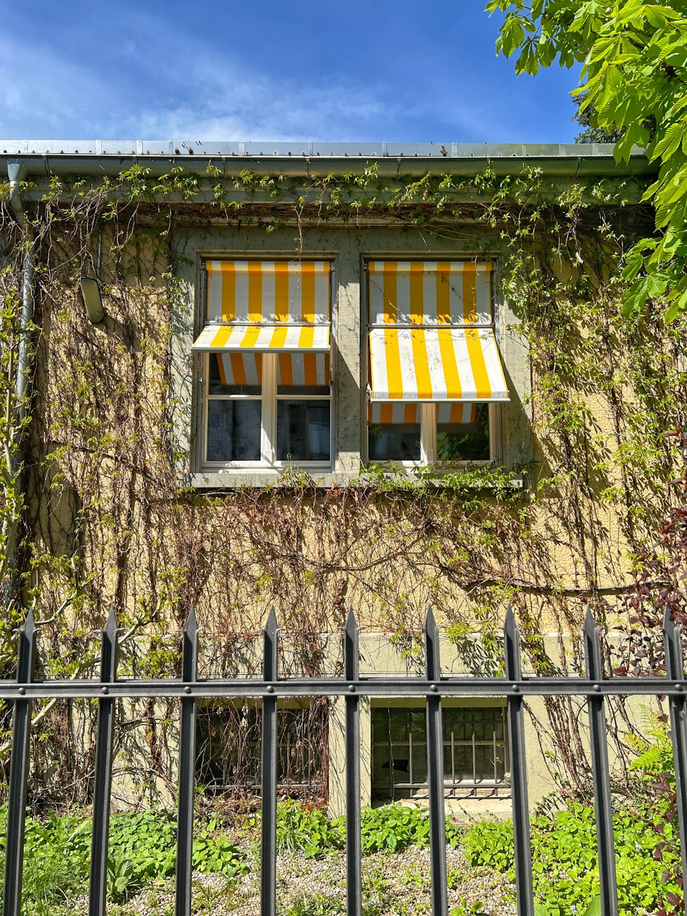 a building with a fence and a window with yellow and white striped awnings