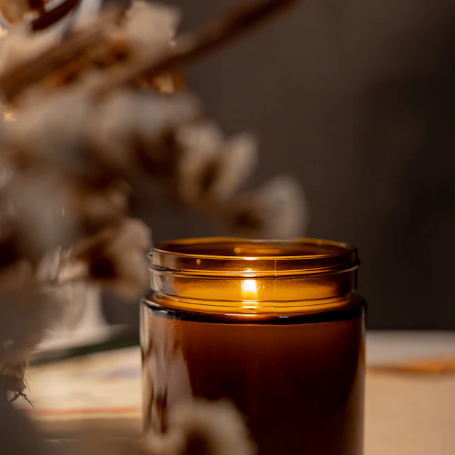 A lit candle in a glass jar sitting on top of a table
