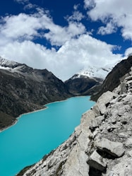 a blue lake surrounded by mountains under a cloudy sky
