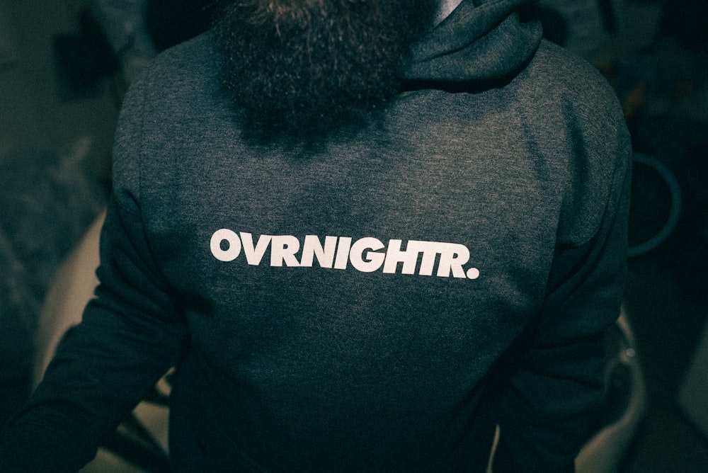 a man with a beard wearing a sweatshirt with the word overnight printed on it