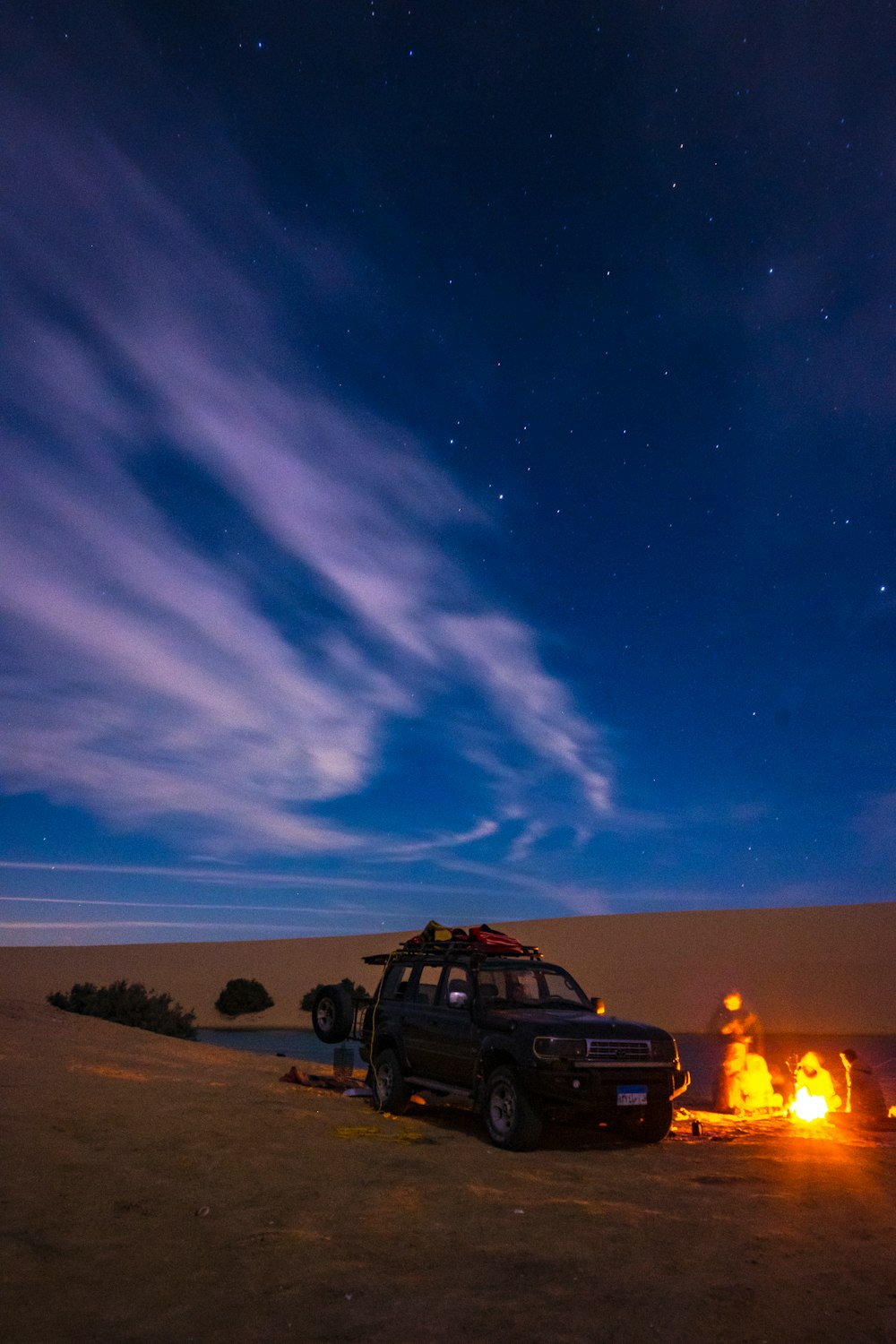 a car is parked in the desert with a campfire