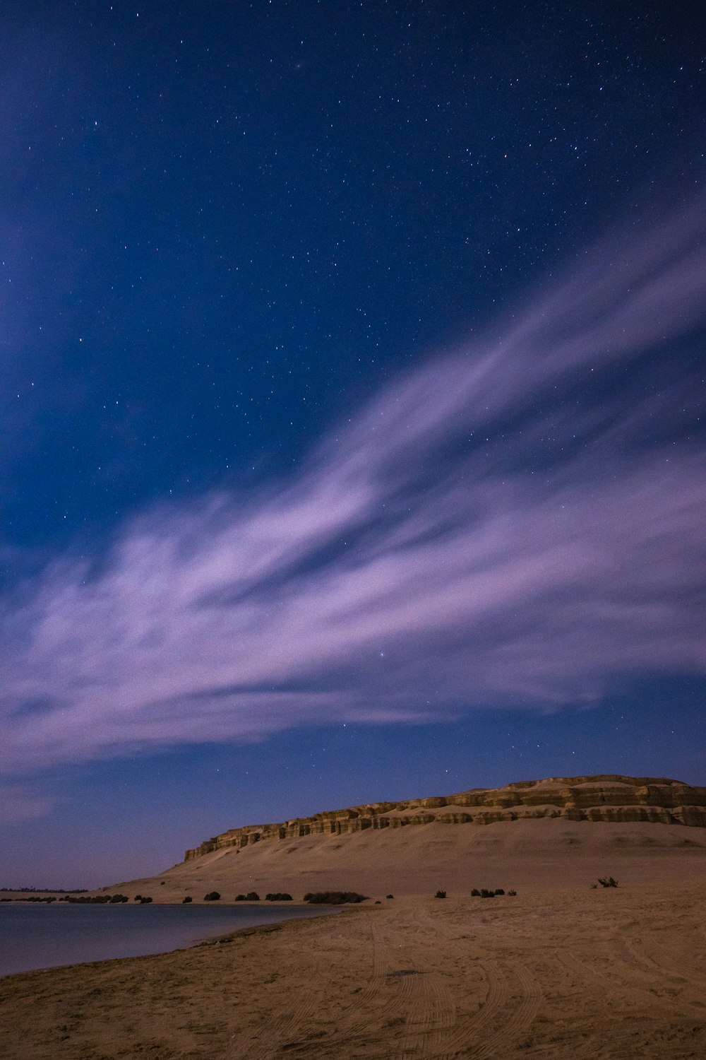 the night sky is lit up over a sandy beach