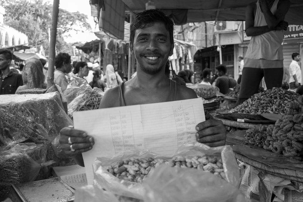 a man holding a paper in front of a bunch of vegetables