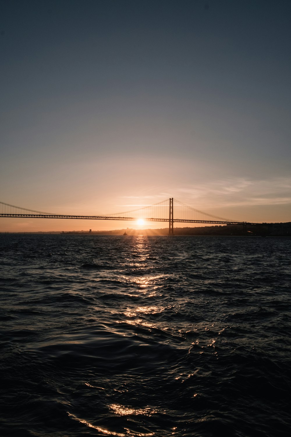 the sun is setting over the water near a bridge