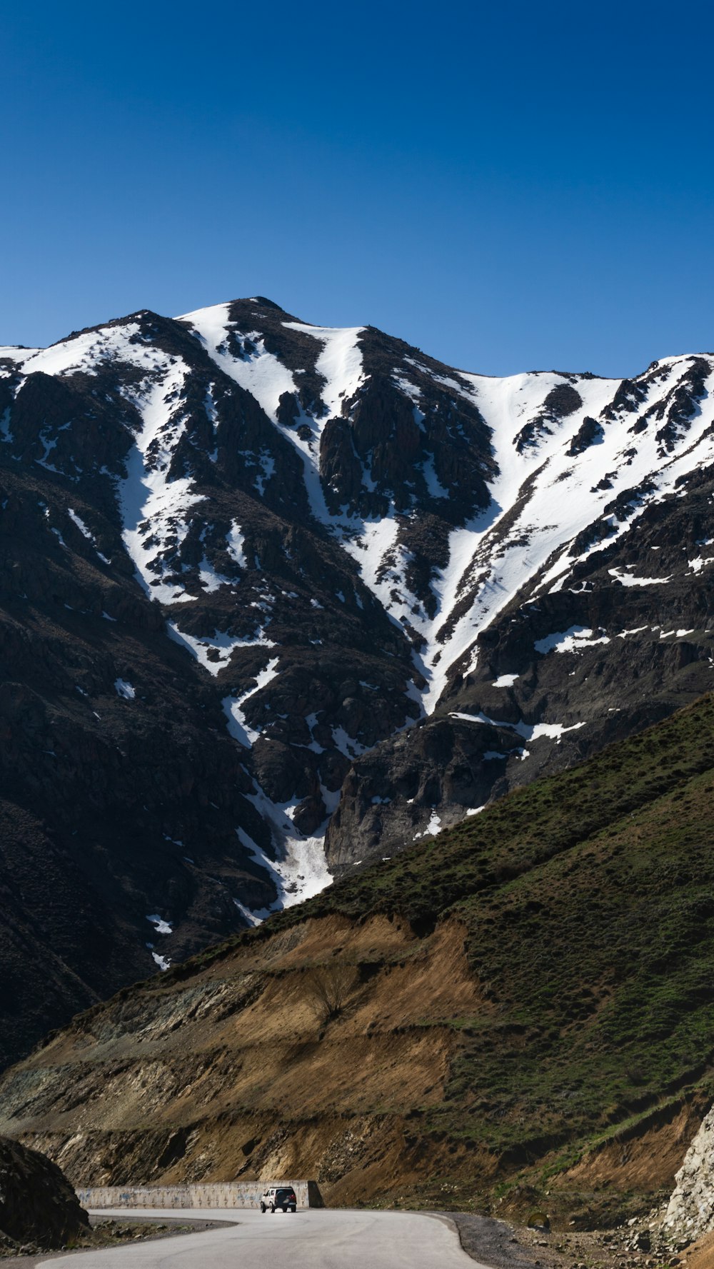 a car driving down a road in front of a snow covered mountain