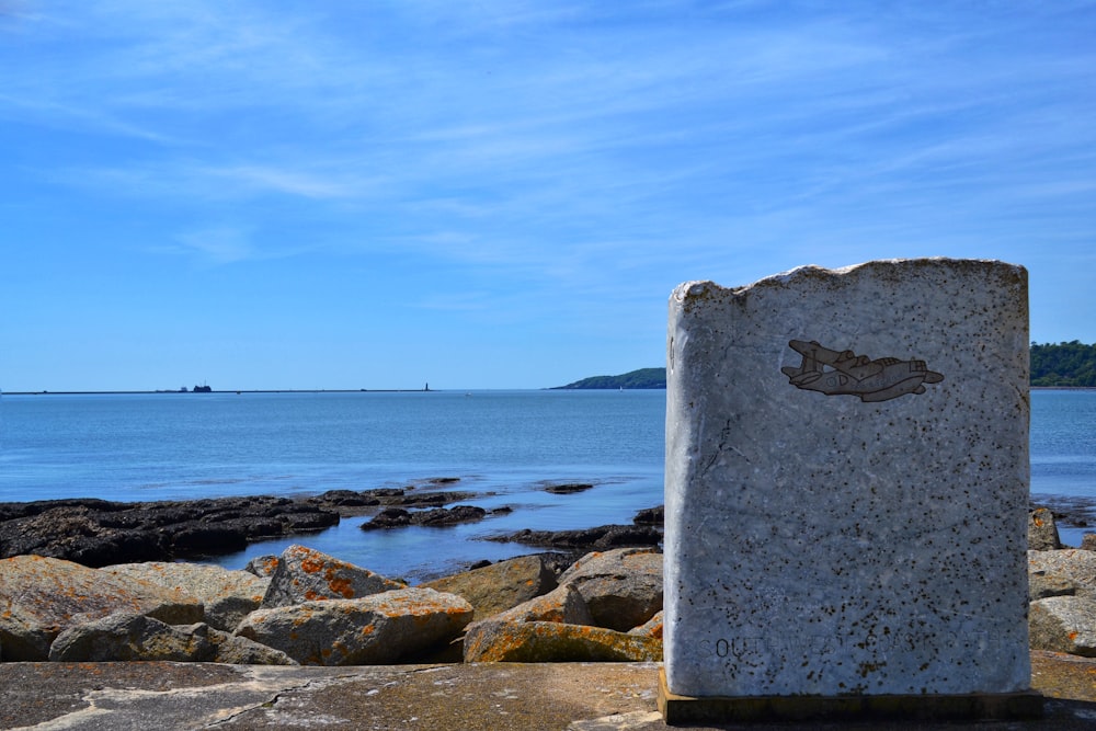 un gros rocher assis au sommet d’une plage à côté de l’océan
