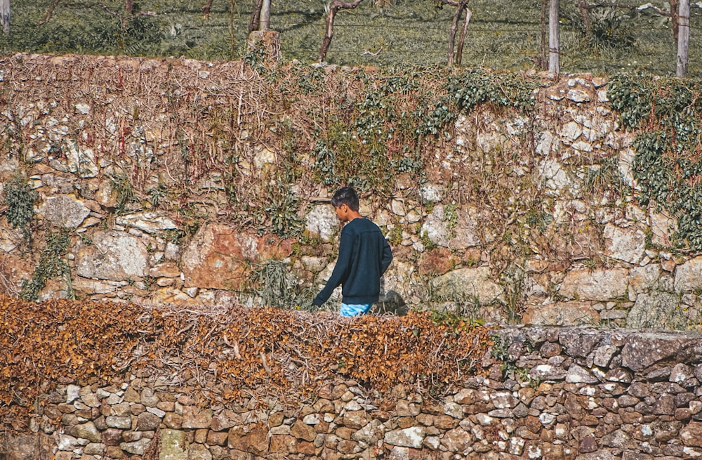 a man walking along a stone wall next to a forest
