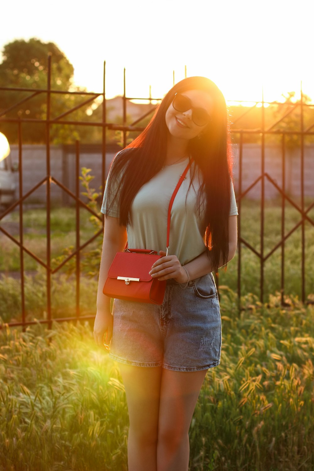 a woman standing in a field holding a red purse