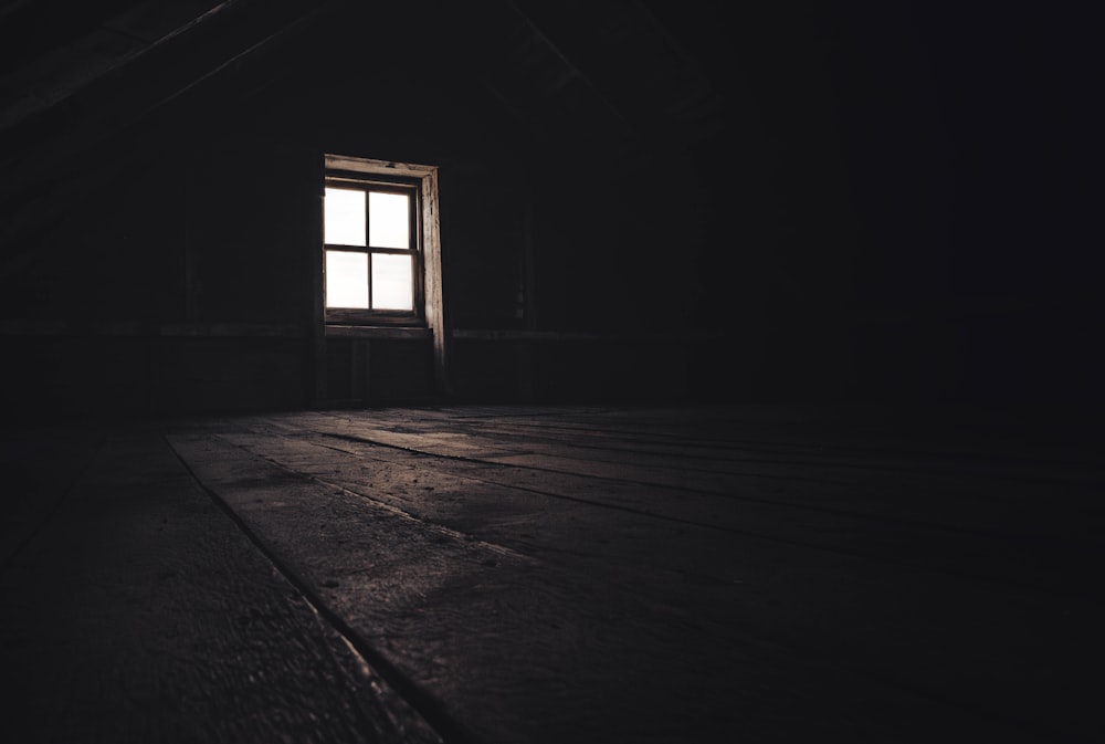 a dark room with a window and a wooden floor