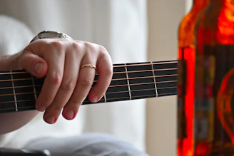 a person playing a guitar with a bottle in the background