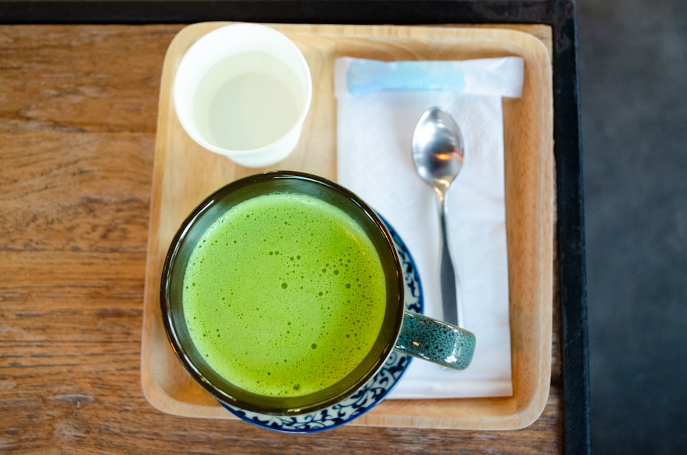 a cup of green liquid and a spoon on a tray