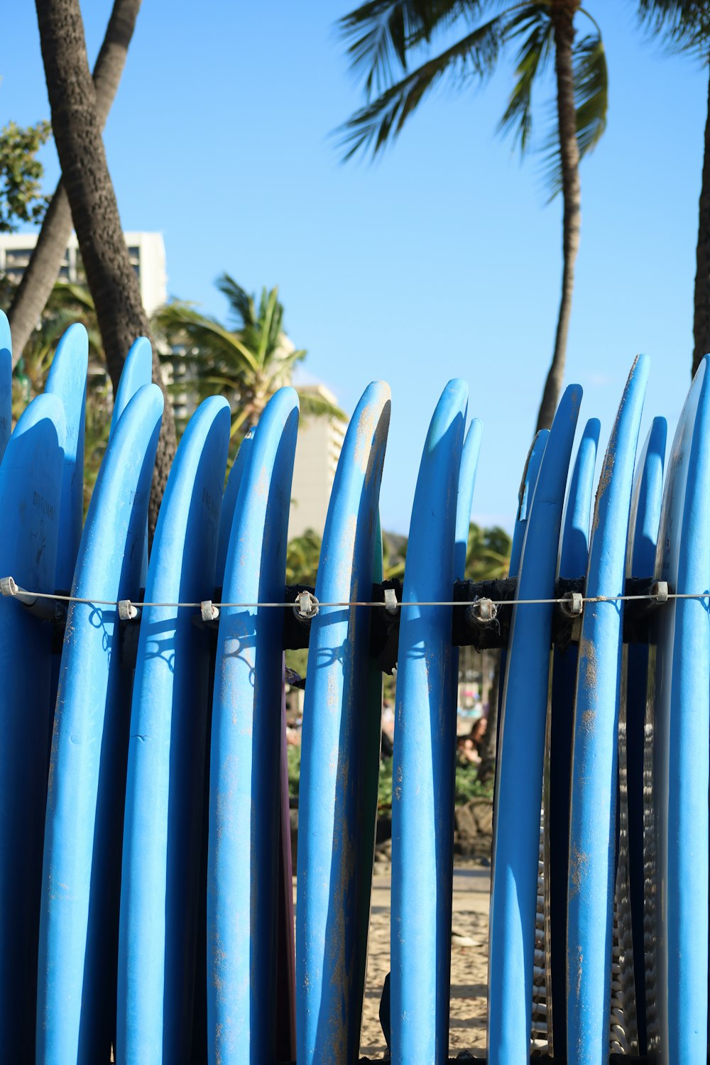 a row of blue surfboards leaning against a fence