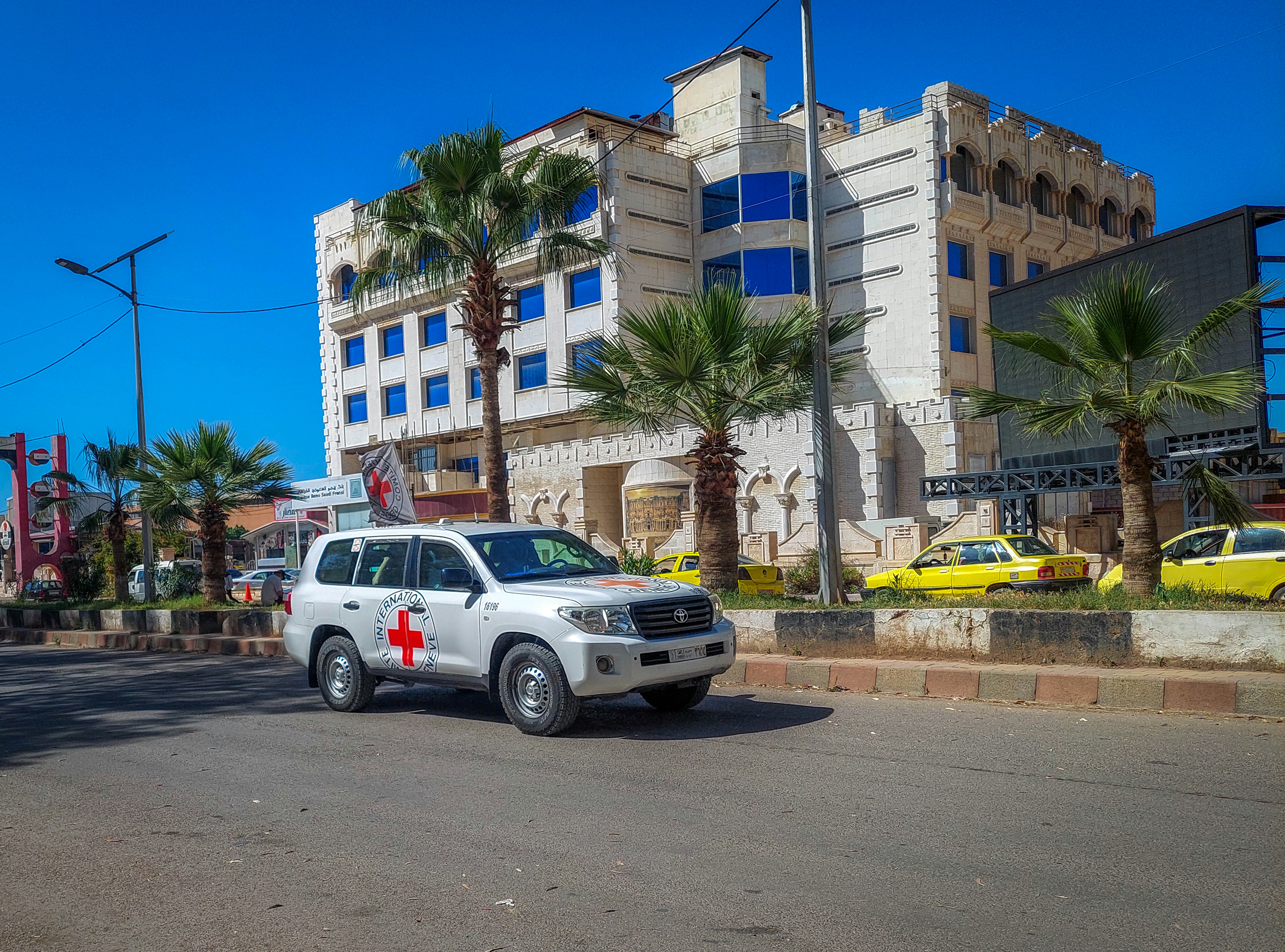 a white suv driving down a street next to a tall building, A picture of the streets of Daraa in 2024