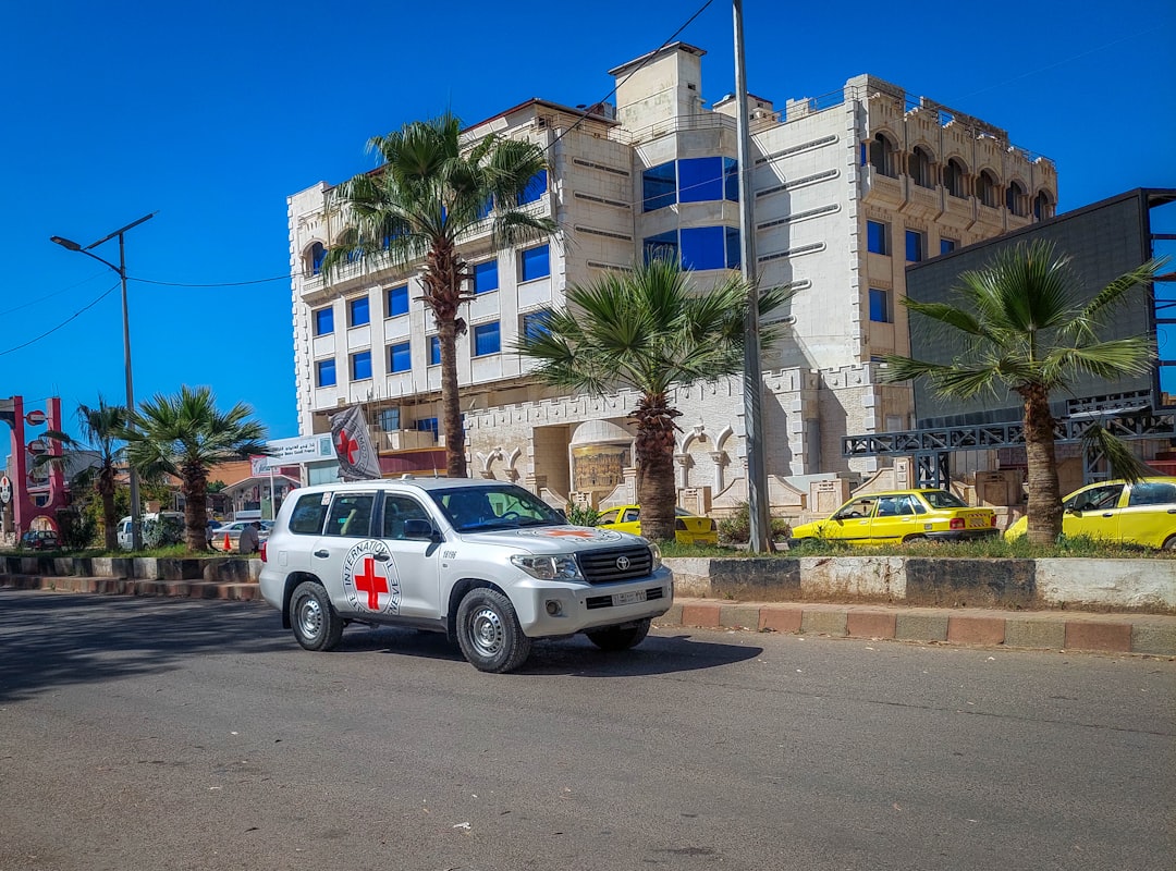 a white suv driving down a street next to a tall building, A picture of the streets of Daraa in 2024