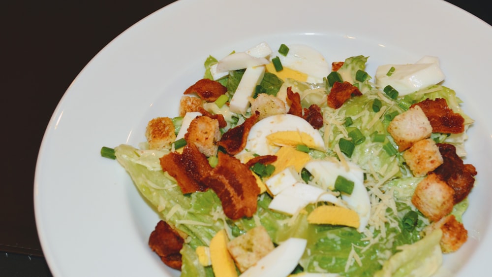 a white plate topped with a salad covered in bacon