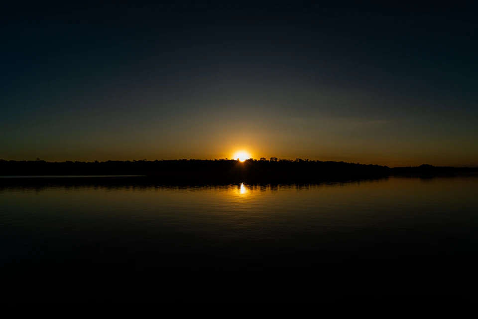 Serene sunset over calm waters reflects vibrant sunset hues behind the horizon line