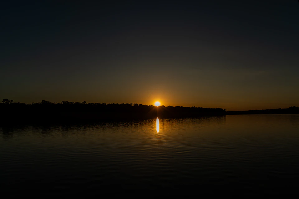 Serene sunset over calm waters with reflected sunlight casting warm glow across sky