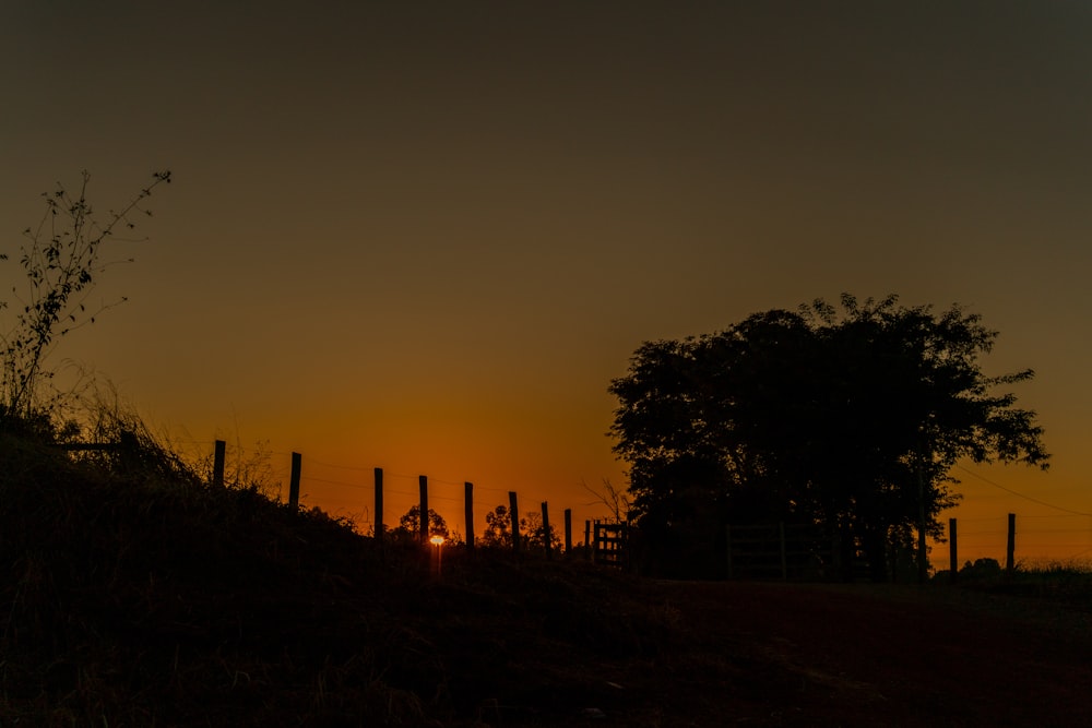 the sun is setting behind a fence on a hill