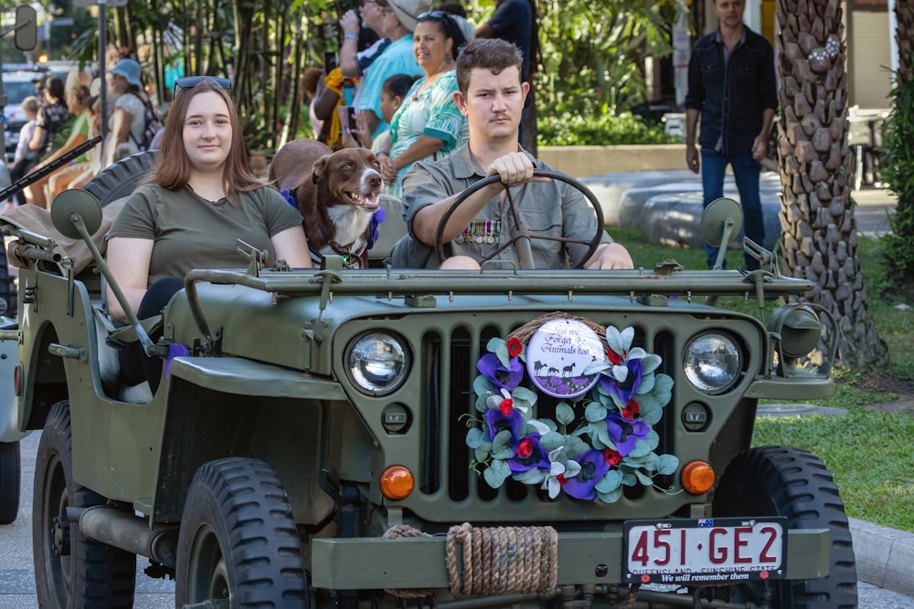 a man and a woman riding in a jeep with a dog