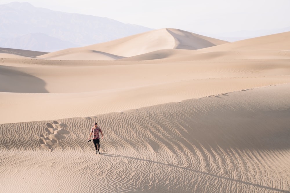 a man walking across a sandy desert with mountains in the background