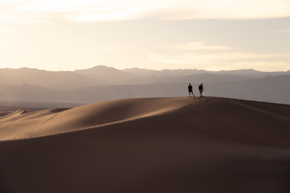 two people standing on top of a sand dune