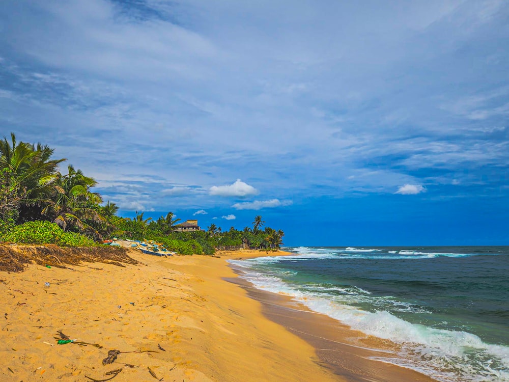a sandy beach next to the ocean under a cloudy blue sky