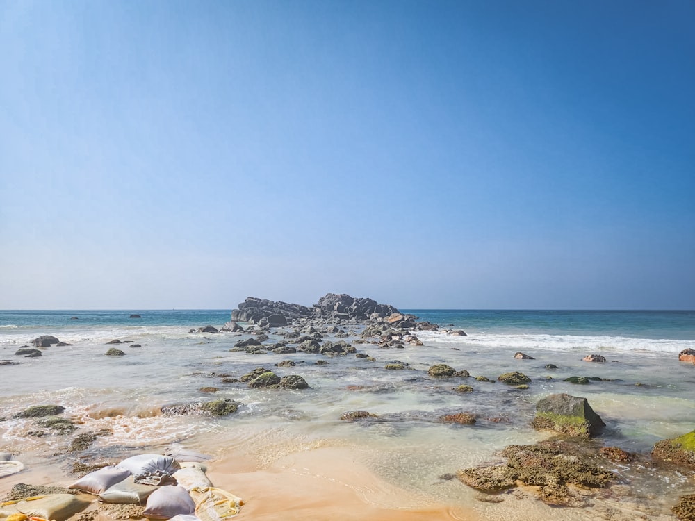 a sandy beach with rocks and water under a blue sky