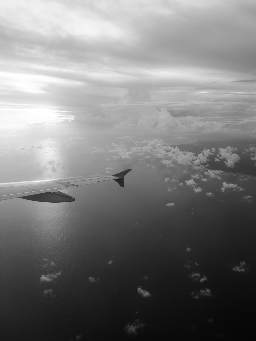an airplane wing flying over the ocean under a cloudy sky
