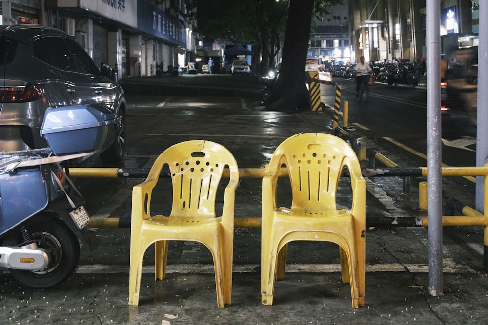 two yellow plastic chairs sitting on the side of a street
