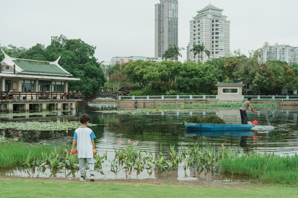 a young boy standing next to a small boat in a lake