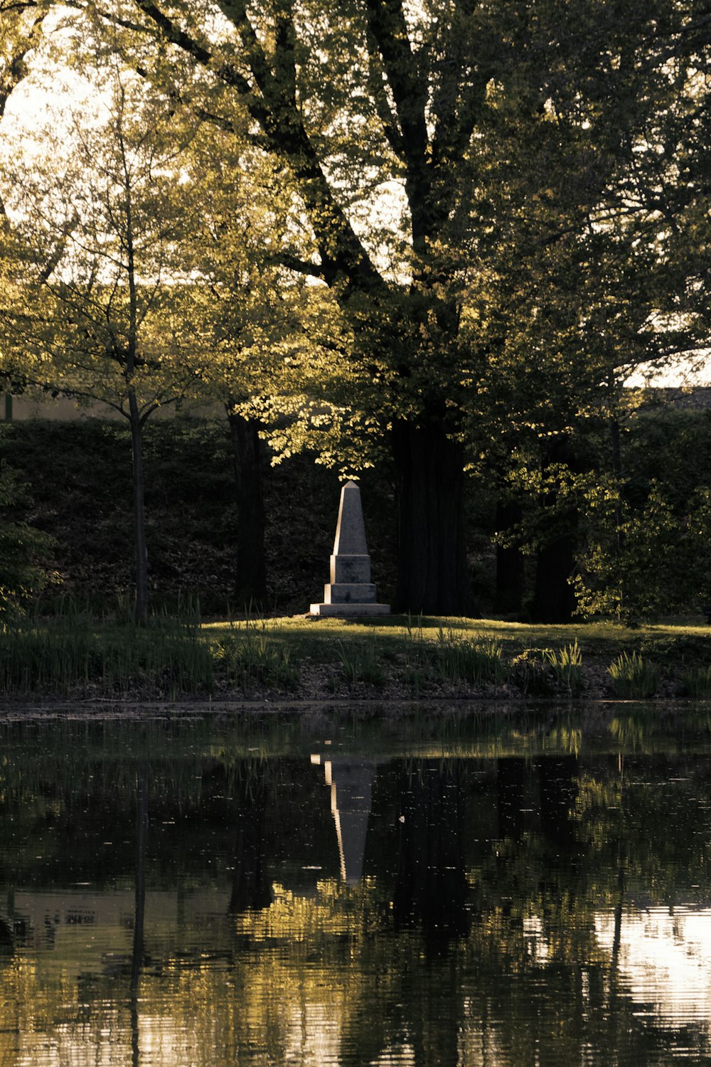 a statue in the middle of a lake surrounded by trees