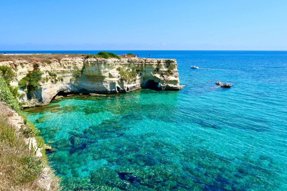 a rocky cliff with clear blue water near a beach