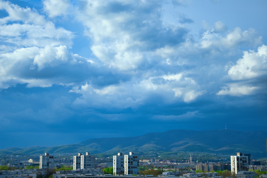 a cloudy sky over a city with mountains in the background,