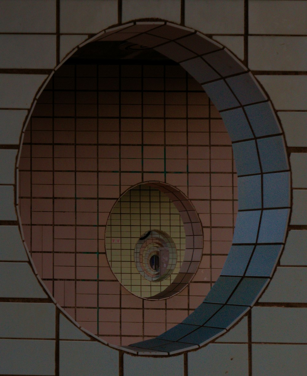 ein runder Spiegel an einer gefliesten Wand über einem Pissoir